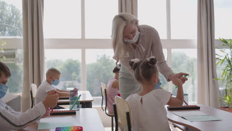 At-school-in-the-classroom-children-write-in-notebooks-in-protective-masks-observing-a-social-distance.-School-education-during-the-pandemic