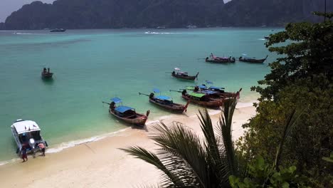 4K-AERIAL-DOLLY-BACKWARD-VIEW-of-a-beach-with-Longtail-boats-moored-in-Phi-Phi-Island-bay,-Drone-Pass-near-tree-in-Phi-Phi-Don,-Thailand