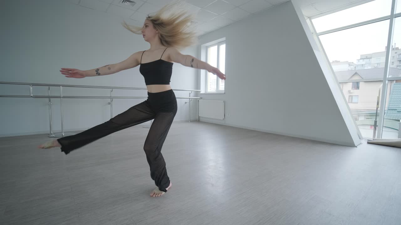 chica en forma con ropa negra actuando contemporáneamente. bailarina muestra movimientos fluidos, cuerpo y manos ondas en la habitación blanca. coreografía de danza de ballet moderno. joven se mueve suavemente