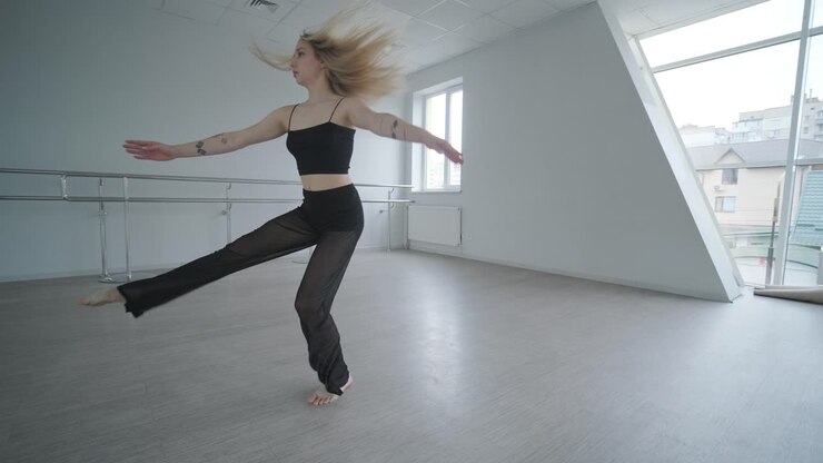 Fit girl in black clothes performing contemporary. Female dancer shows flowing motions, body and hands waves at white room. Modern ballet dance choreography. Young woman is moving smoothly