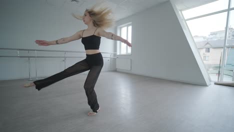 fit girl in black clothes performing contemporary. female dancer shows flowing motions, body and hands waves at white room. modern ballet dance choreography. young woman is moving smoothly