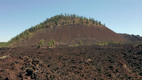 Tiro-Deslizante-Bajo-Sobre-Flujos-De-Lava-Seca-Y-Rugosa-Mirando-Hacia-Un-Cono-De-Ceniza