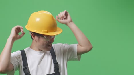 close up of asian man worker wearing goggles and safety helmet singing and dancing while standing in the green screen background studio