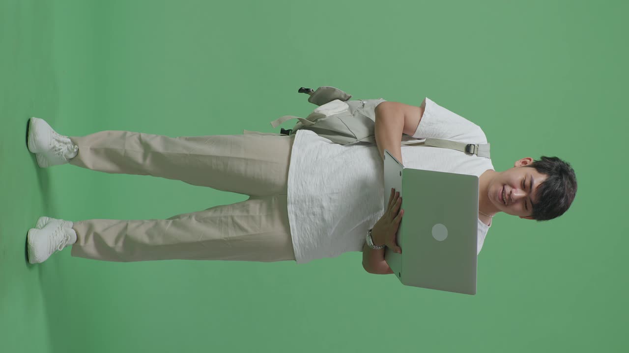 cuerpo lleno de un hombre asiático sonriente estudiante usando una computadora portátil en el estudio de pantalla verde