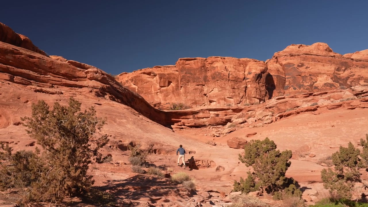 Uomo sul sentiero escursionistico Funnel Arch nel paesaggio desertico dello Utah con scenografiche formazioni di arenaria rossa, Moab USA