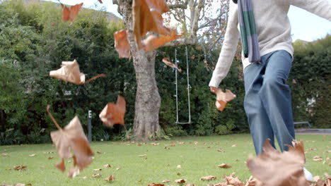 happy african american boy in scarf playing with leaves in garden, slow motion