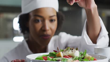 african american female chef garnishing dish and similing in restaurant kitchen