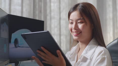 close up side view of asian female automotive designer comparing the 3d model of ev car on the desktop computers to the photo on her tablet in the studio