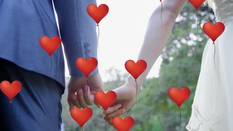 multiple heart balloons floating against mid section of newly married couple holding pinky finger