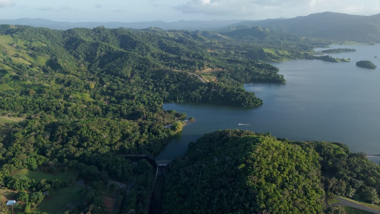 Panoramic drone shot of green mountain landscape with water reservoir of Hatillo Dam. Sunny day with blue sky, Dominican Republic.