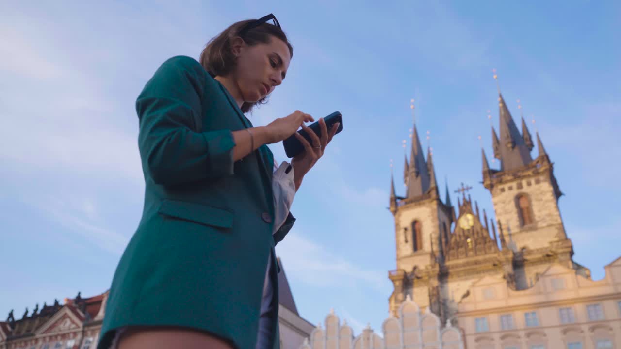 Donna che scorre il telefono, con la Chiesa di Nostra Signora di Týn sullo sfondo, a Praga.