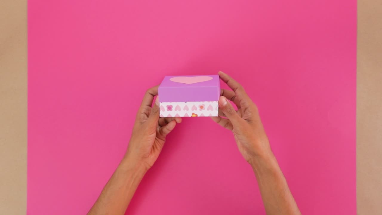 Hands hold a decorated Valentines Day candy box over a vibrant pink background