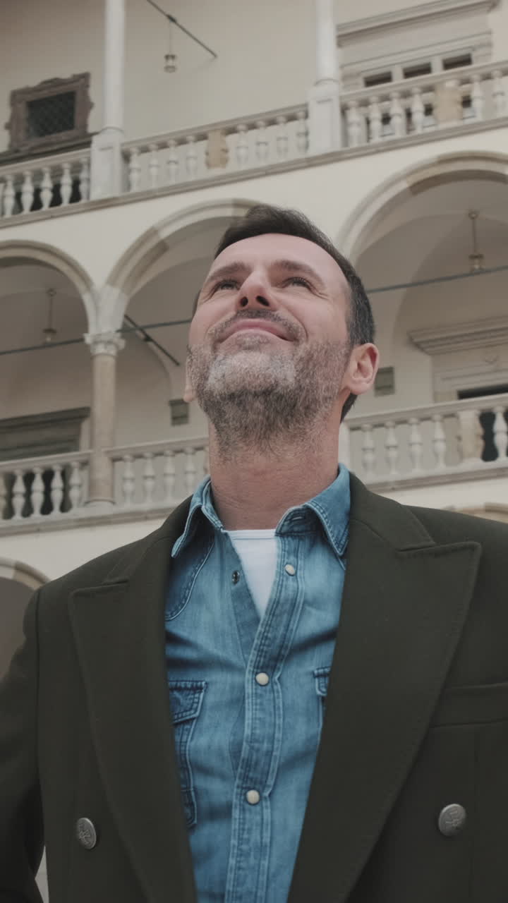 Uomo con cappotto e camicia di jeans che guarda un edificio