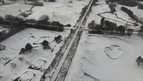 conducción de automóviles en una carretera cubierta de nieve rodeada por un campo de golf durante el invierno