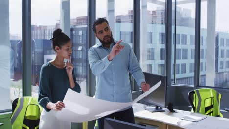 dos colegas masculinos y femeninos diversos con un plano arquitectónico y discutiendo