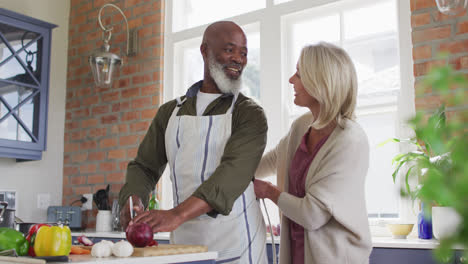 Mujer-Mayor-Caucásica-Atando-Delantal-A-Su-Marido-En-La-Cocina-De-Casa