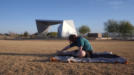 Red hair male doing stretches in a park with an amphitheater behind them.