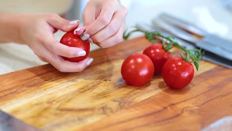close-up of hands removing stems from ripe tomatoes on a wooden board. bright lighting enhances the vibrant red color