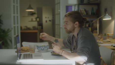 man having breakfast and using laptop at home