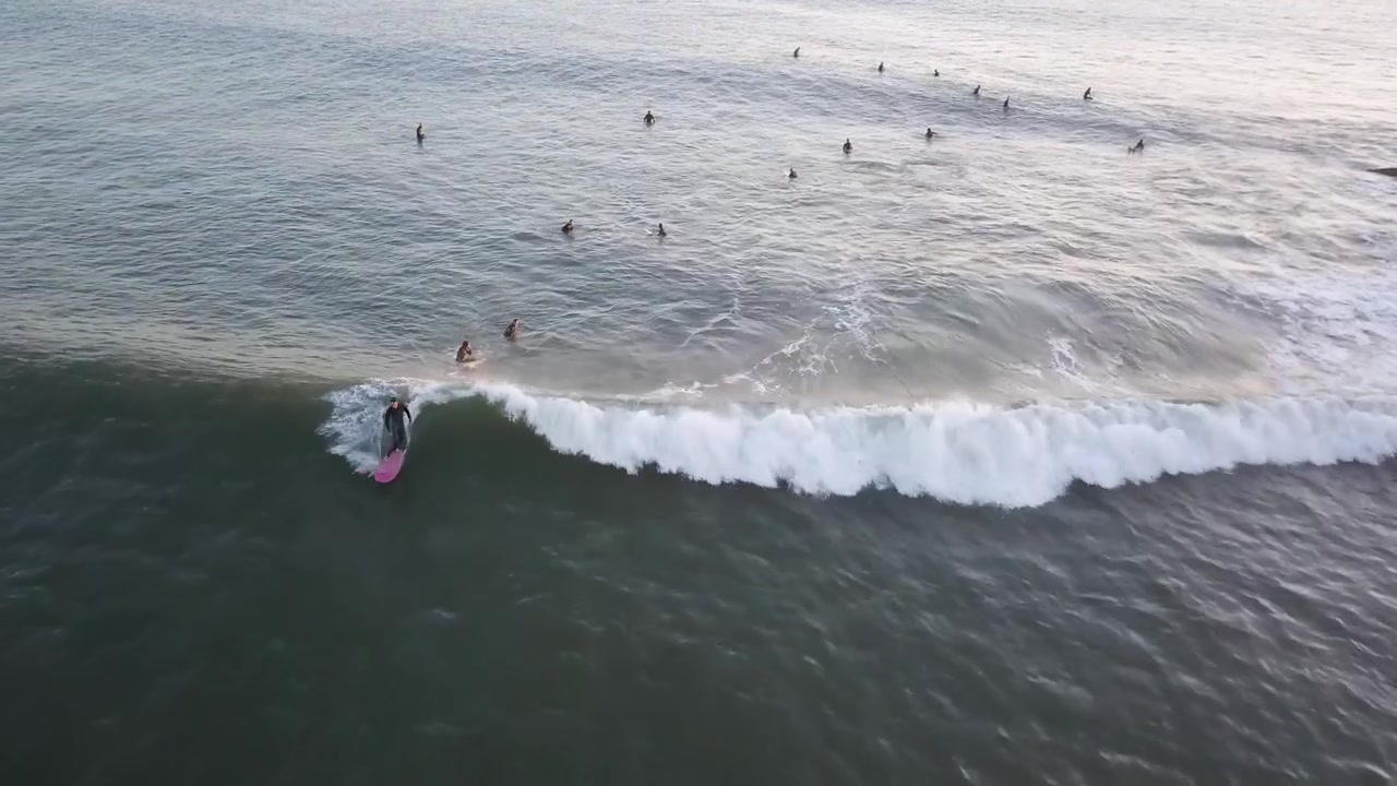 Vista aerea di un giovane surfista che cavalca un'onda oceanica su una longboard al tramonto, Estoril, Cascais.