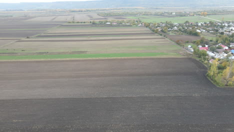 Panorámica-Aérea-De-Drones-Hacia-Arriba-Para-Revelar-Un-Pequeño-Pueblo-Rural-Rodeado-De-Prados-Verdes-Marrones