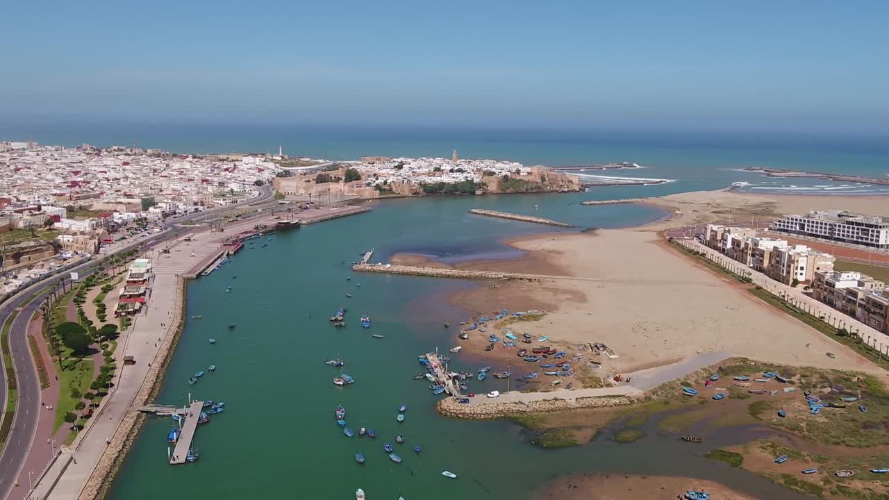 Ripresa panoramica con drone che cattura l'estuario del fiume Bou Regreg tra Rabat e Salé. Mostra il porto turistico, la Kasbah degli Oudaia e il moderno sviluppo urbano lungo la costa atlantica.