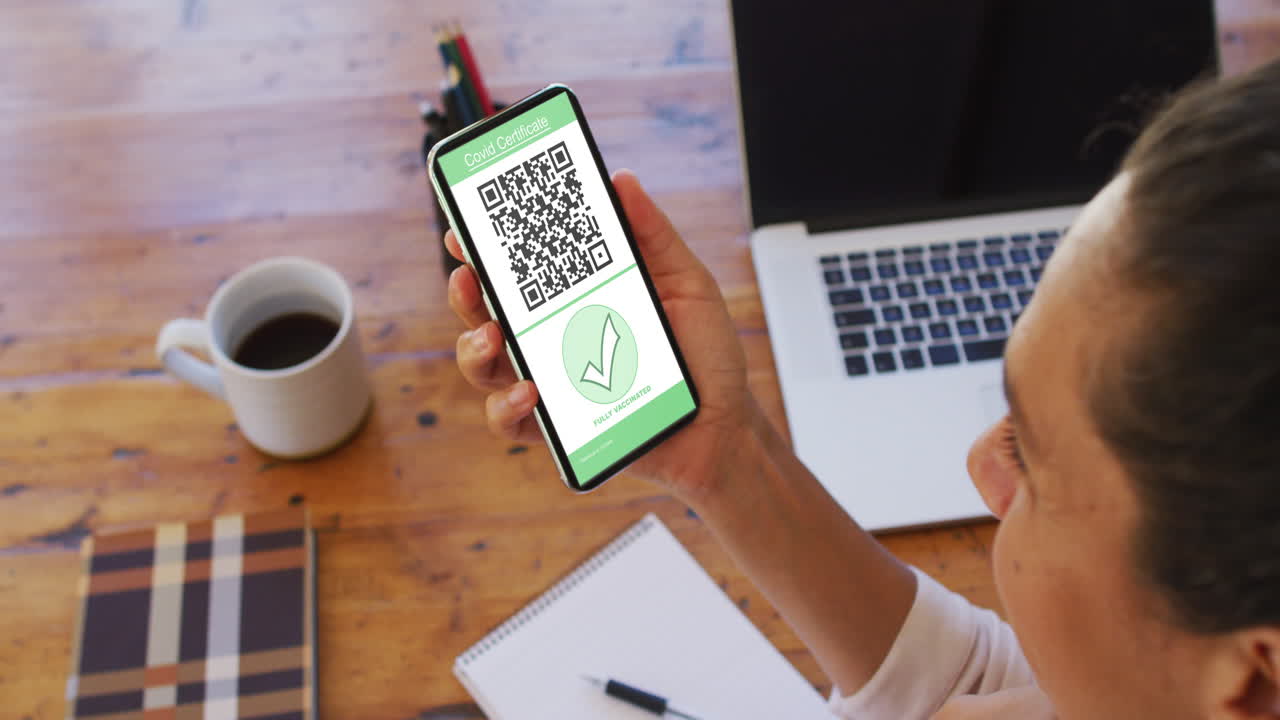 Woman at holding smartphone with covid vaccination certificate and qr code on screen
