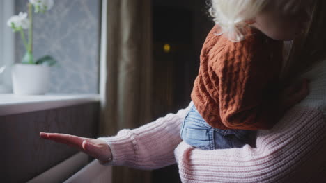 mother cuddling son trying to keep warm by radiator at home during cost of living energy crisis