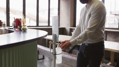 caucasian man working at a bar, using hand sanitising gel dispenser