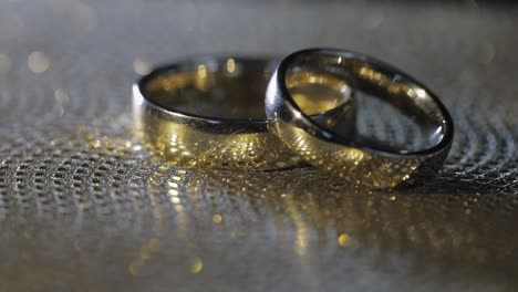 wedding rings lying, rotate, spinning on shiny golden shining surface with light, close-up macro