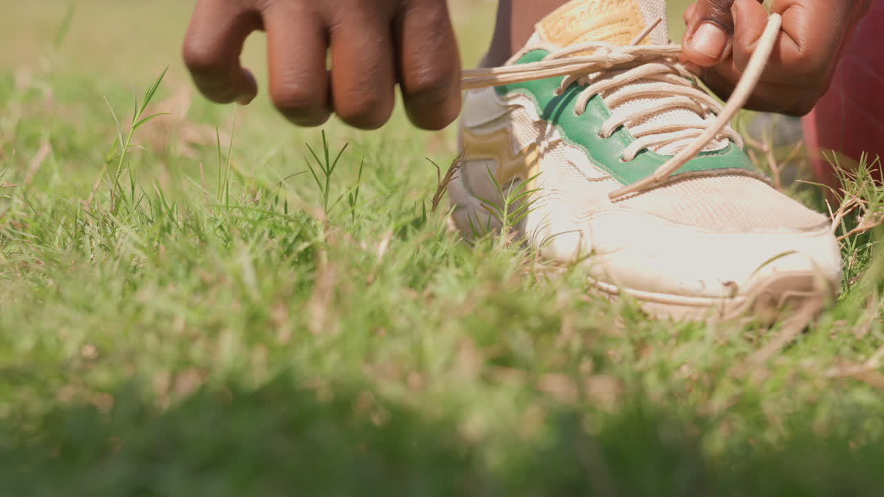 Atleta che si allaccia le scarpe all'aperto. Giovane concorrente che prepara l'attrezzatura al sole. Giovane partecipante sportivo concentrato che si allaccia le scarpe, circondato dalla luce solare naturale e da un ambiente vibrante