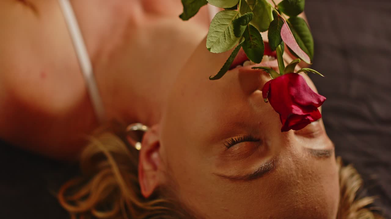 una rosa roja acaricia suavemente el rostro de una hermosa mujer vestida con lencería seductora