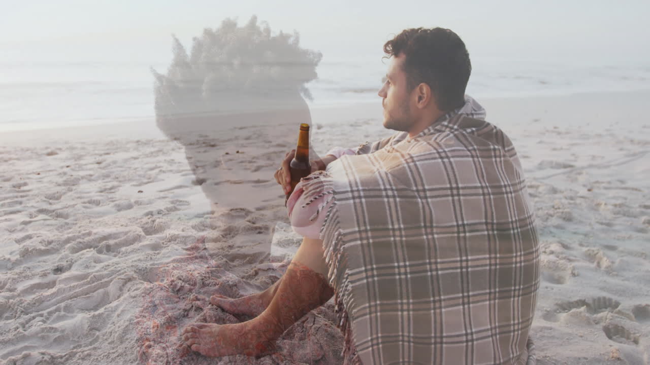Sitting on beach, man wrapped in blanket, animation overlay of another person