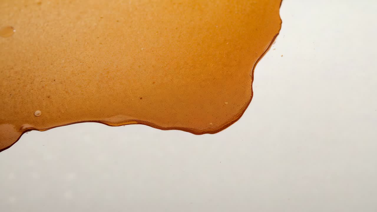 Spreading viscous brown film shifting across white plate, surface tension forming meniscus bubbles