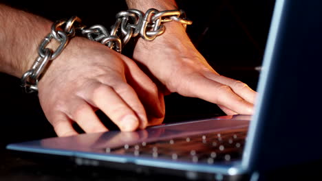 close-up of chained male hands by laptop keyboard, unable to write