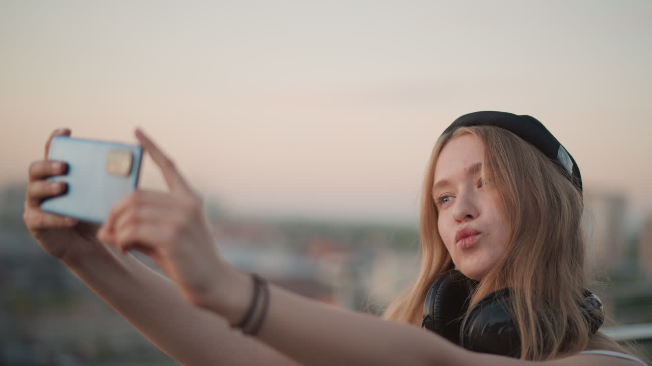 Ballerina felice al tramonto su un tetto, skyline urbano e balli energici durante l'ora d'oro, donna con cuffie che balla spensierata su un tetto con vista sulla città al tramonto con un sorriso smagliante