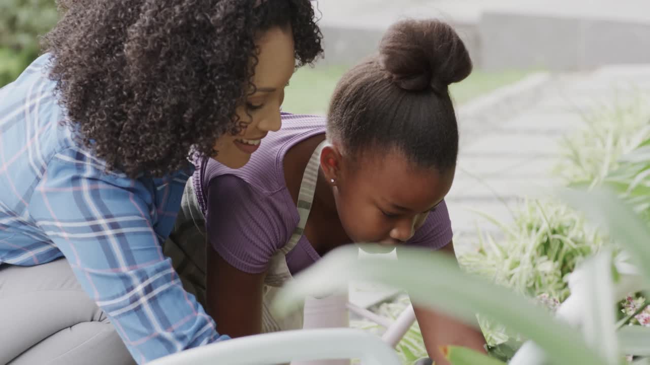Happy african american mother and daughter planting flowers in garden, slow motion, unaltered