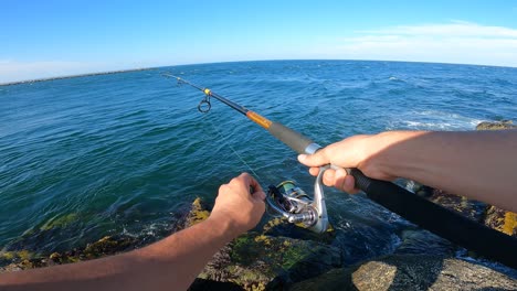 Person-spin-fishing-on-rocky-ocean-coastline,-POV-view