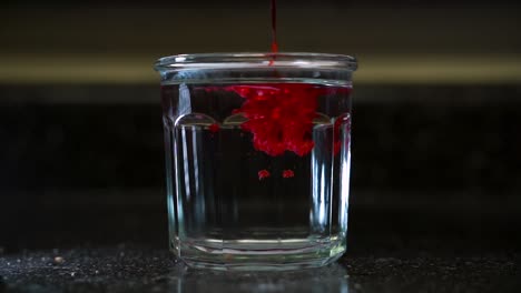 hot melted red wax poured into cold glass of clear water