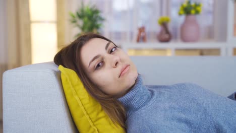 Thoughtful-young-woman-resting-on-sofa-at-home-looking-at-camera.