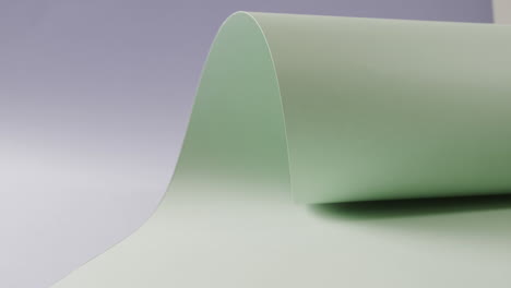 Close-up-of-pale-green-rolled-piece-of-paper-on-blue-background-with-copy-space-in-slow-motion