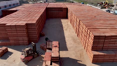 Revealing-shot-of-construction-factory-with-bricks-stacked-and-forklifts-loading-bricks-on-lories-for-export