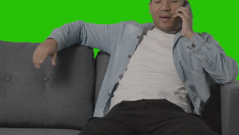 Close-Up-Of-Young-Man-Sitting-On-Sofa-Talking-On-Mobile-Phone-Against-Green-Screen-