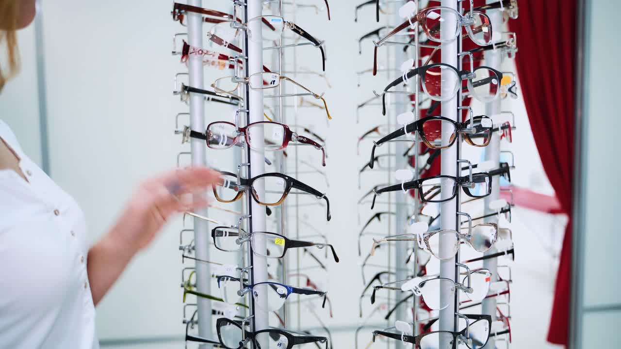 Pretty young woman is choosing new glasses at optical store. Beautiful lady choosing eyeglasses from stand at optics.