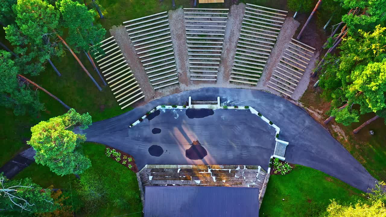 Open-air wooden seating amphitheater in pine forest lit by evening sunlight Aerial drone video