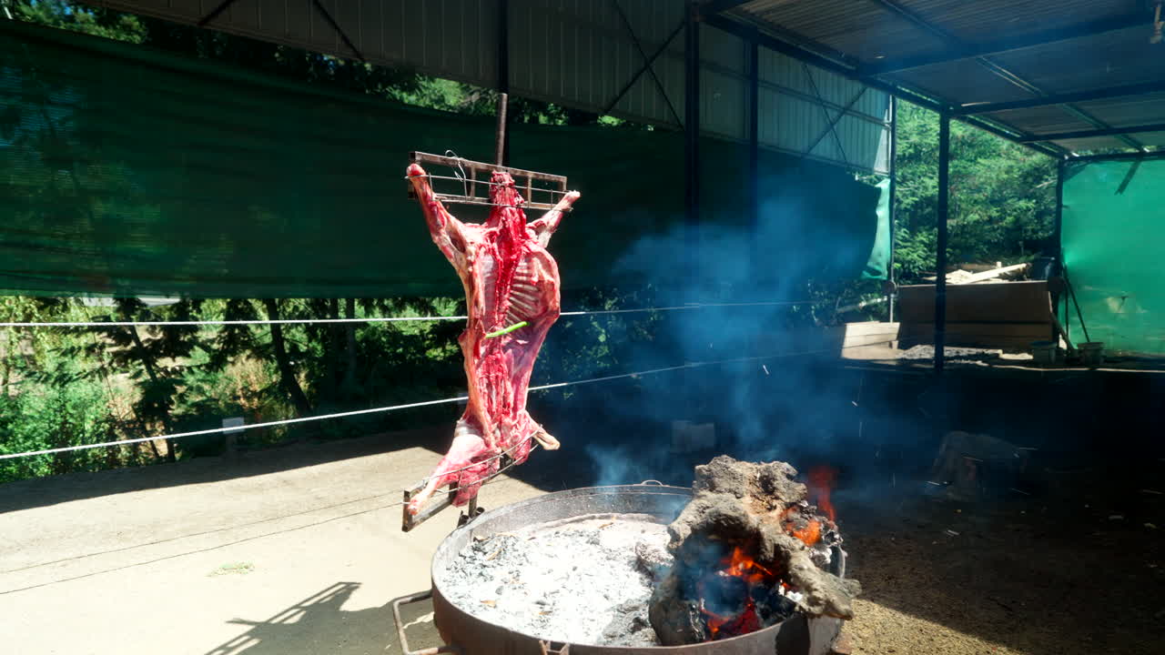 Whole lamb carcass roasting vertically over open fire pit in rustic outdoor grill setting, capturing traditional meat preparation methods and barbecue culture