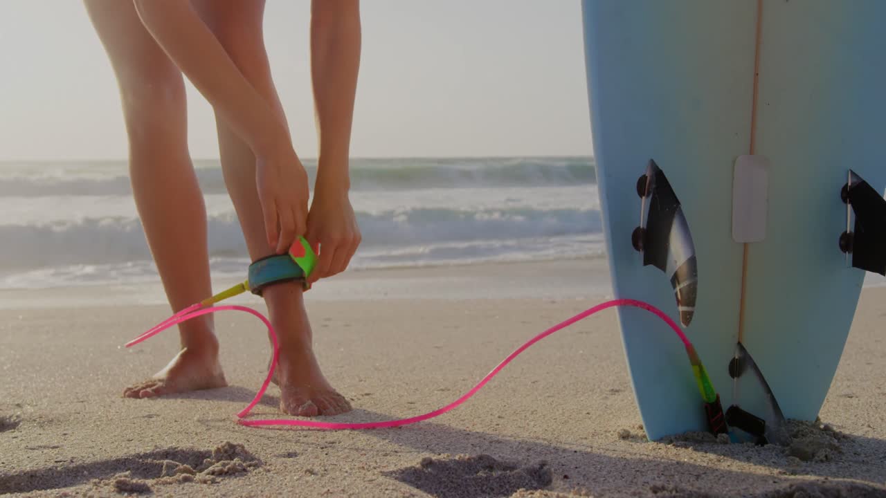 mujer atando la correa de la tabla de surf en la playa al sol 4k
