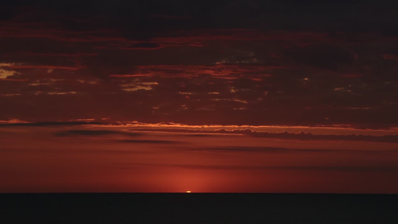 Time lapse of a bright red and orange sunset over the ocean, with few clouds