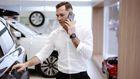 young man using phone while chooses a new model of a luxury car in showroom