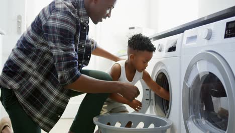 side view of black father and son washing clothes in washing machine at comfortable home 4k